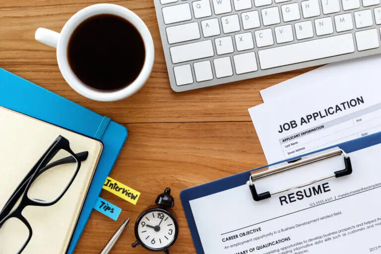 Overhead view of a desk with a job application, resume, interview tips, keyboard, and coffee.